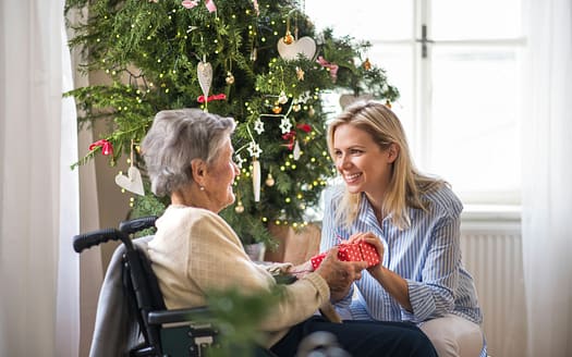 Health visitor and senior woman in wheelchair with a present at home at Christmas.